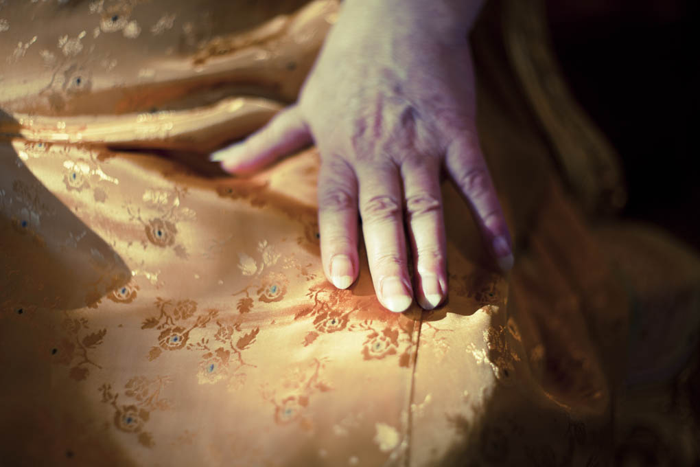 A close up of hands resting on the lap of a woman in a gold satin dress.